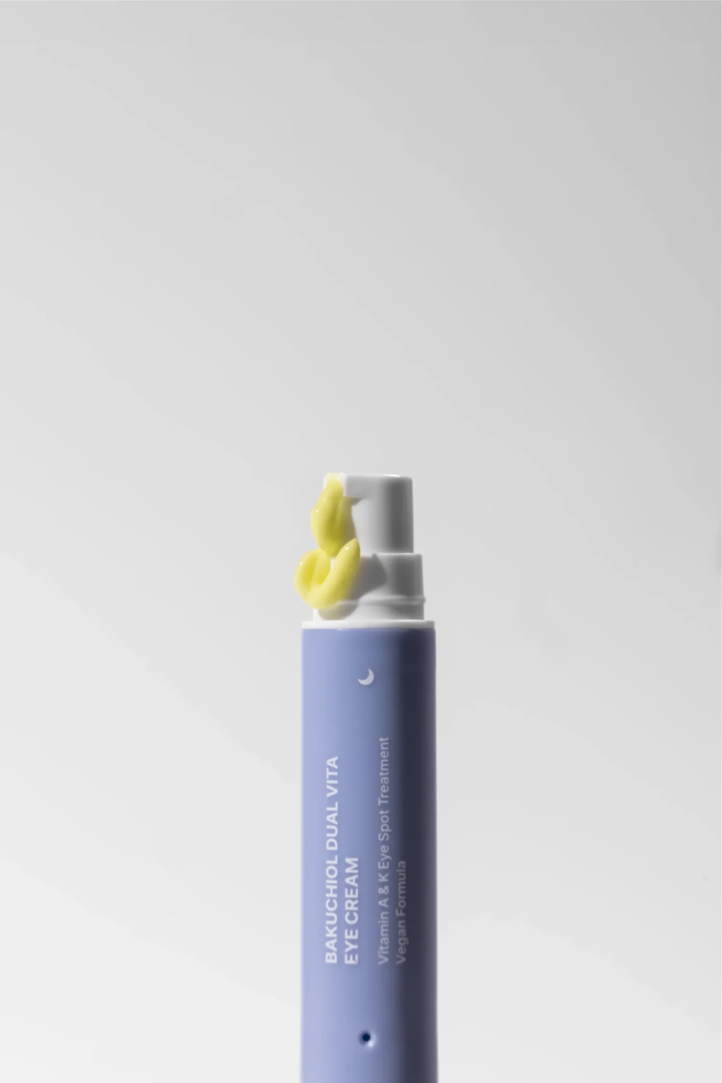 Close up of Herbloom's Bakuchiol Dual Vita Eye Cream night end of the stick, with yellow cream coming out of the pump, against a light grey background. Available for purchase at Sinless Skincare.