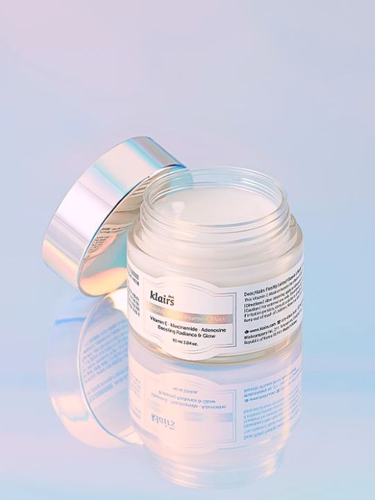 Klairs Freshly Juiced Vitamin E Mask jar with lid off, standing on a pastel blue reflective surfance