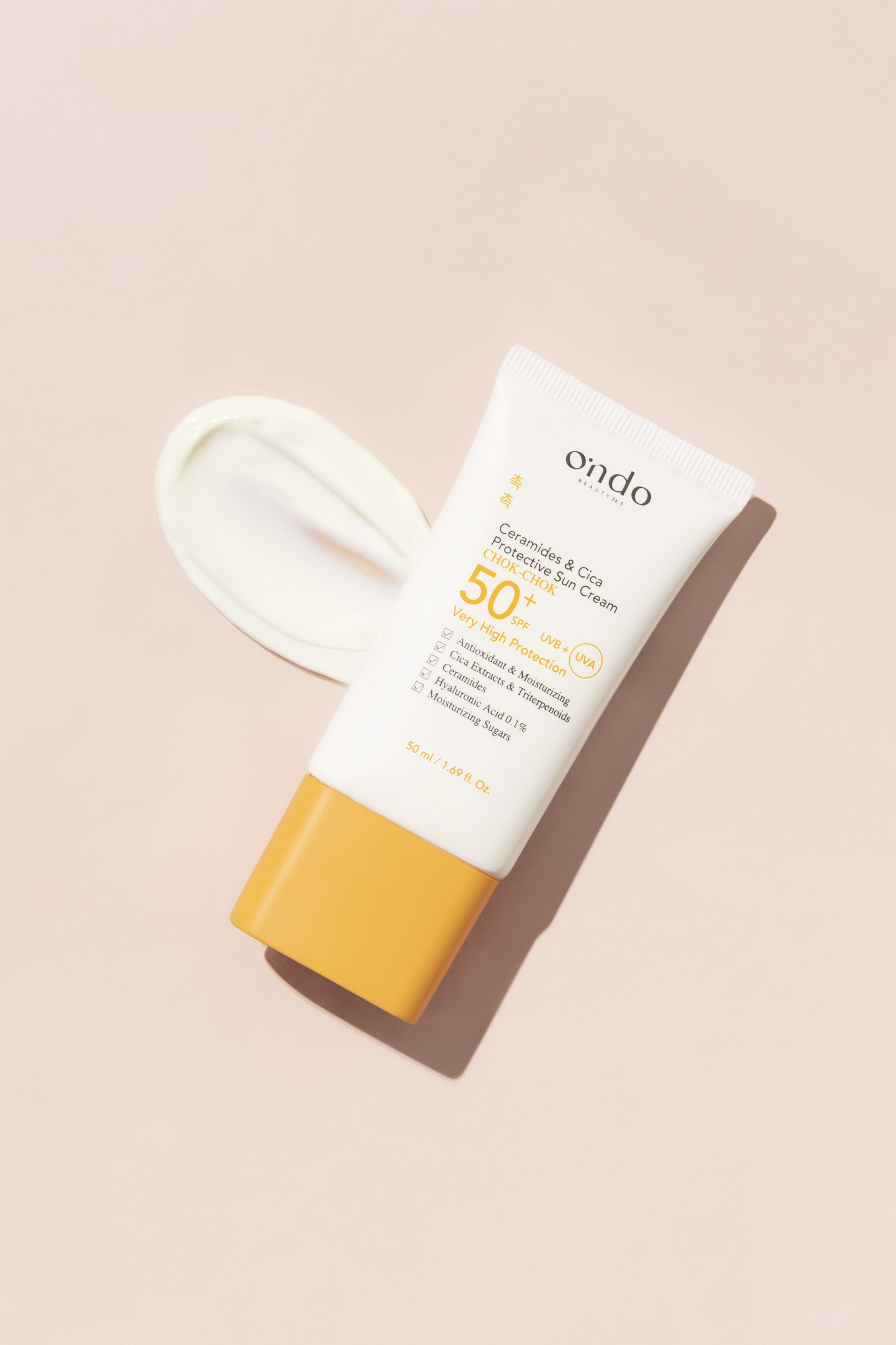 Aerial view of Ondo Beauty 36.5's Ceramides & Cica Protective Sun Cream tube with a smear of cream next to it, against a beige background.