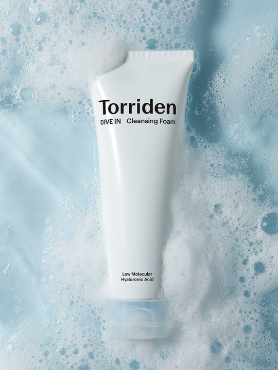 Tube of Torriden Dive In Cleansing Foam lying face up, surrounded by foaming water. Available at Sinless Skincare.