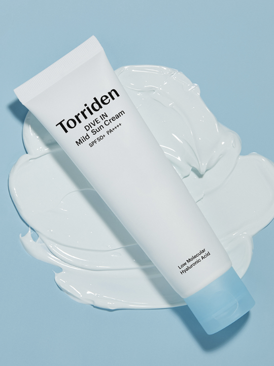 Aerial view of Torriden Dive In Mild Sun Cream 60ml tube lying on a patch of white cream against a blue background. Available at Sinless Skincare.