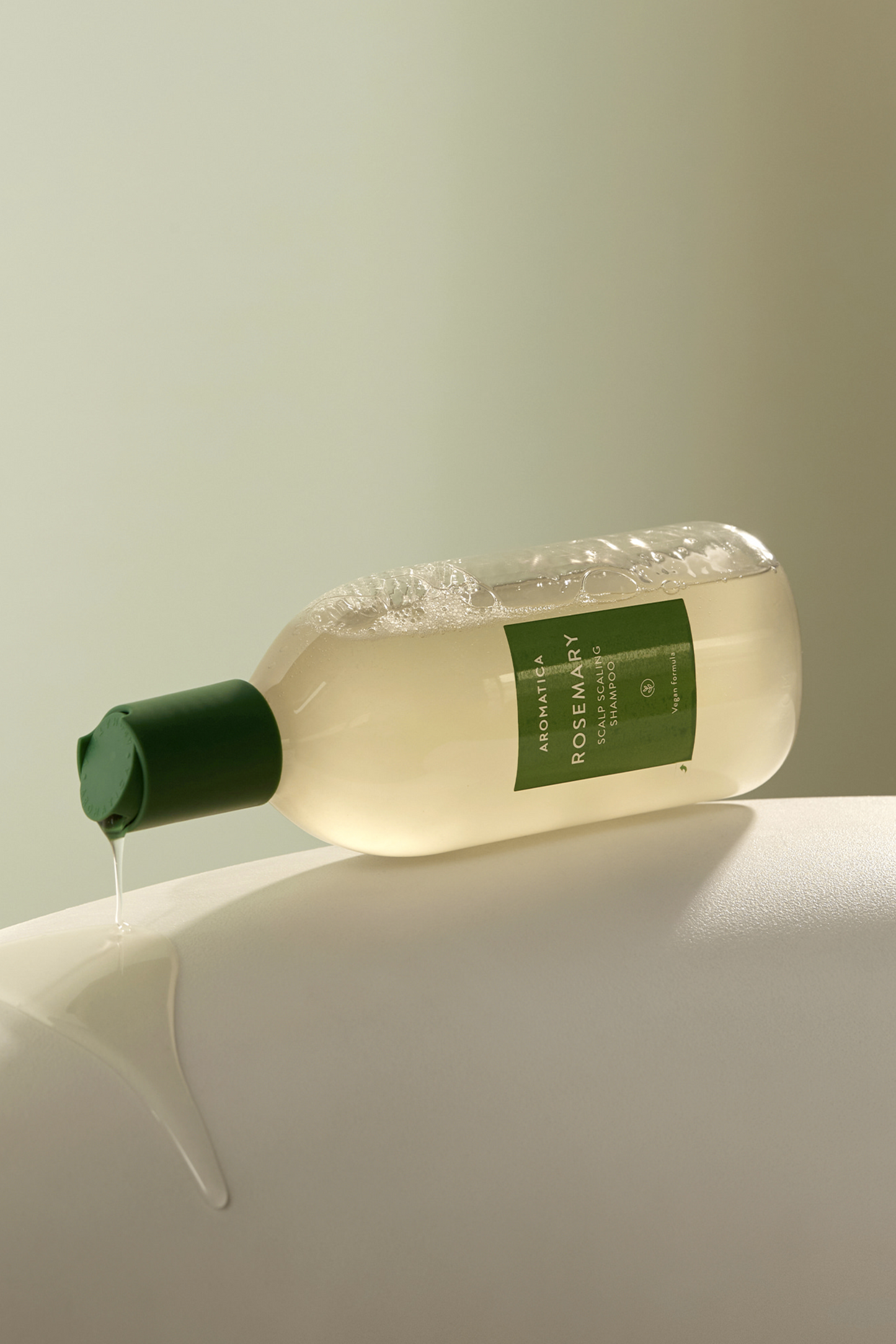 400ml bottle of Aromatica's Rosemary Scalp Scaling Shampoo tipped on its side with shampoo dripping down from its cap.