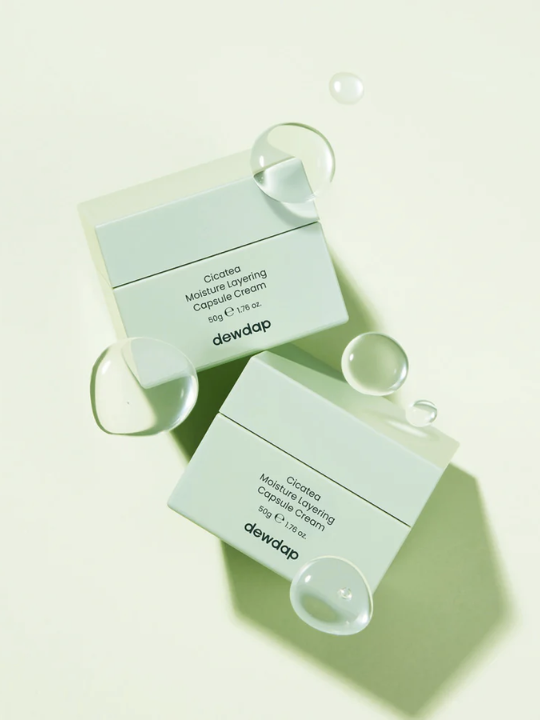 Two containers of Dewdap Cicatea Moisture Layering Capsule Cream on a light green background with bubbles.