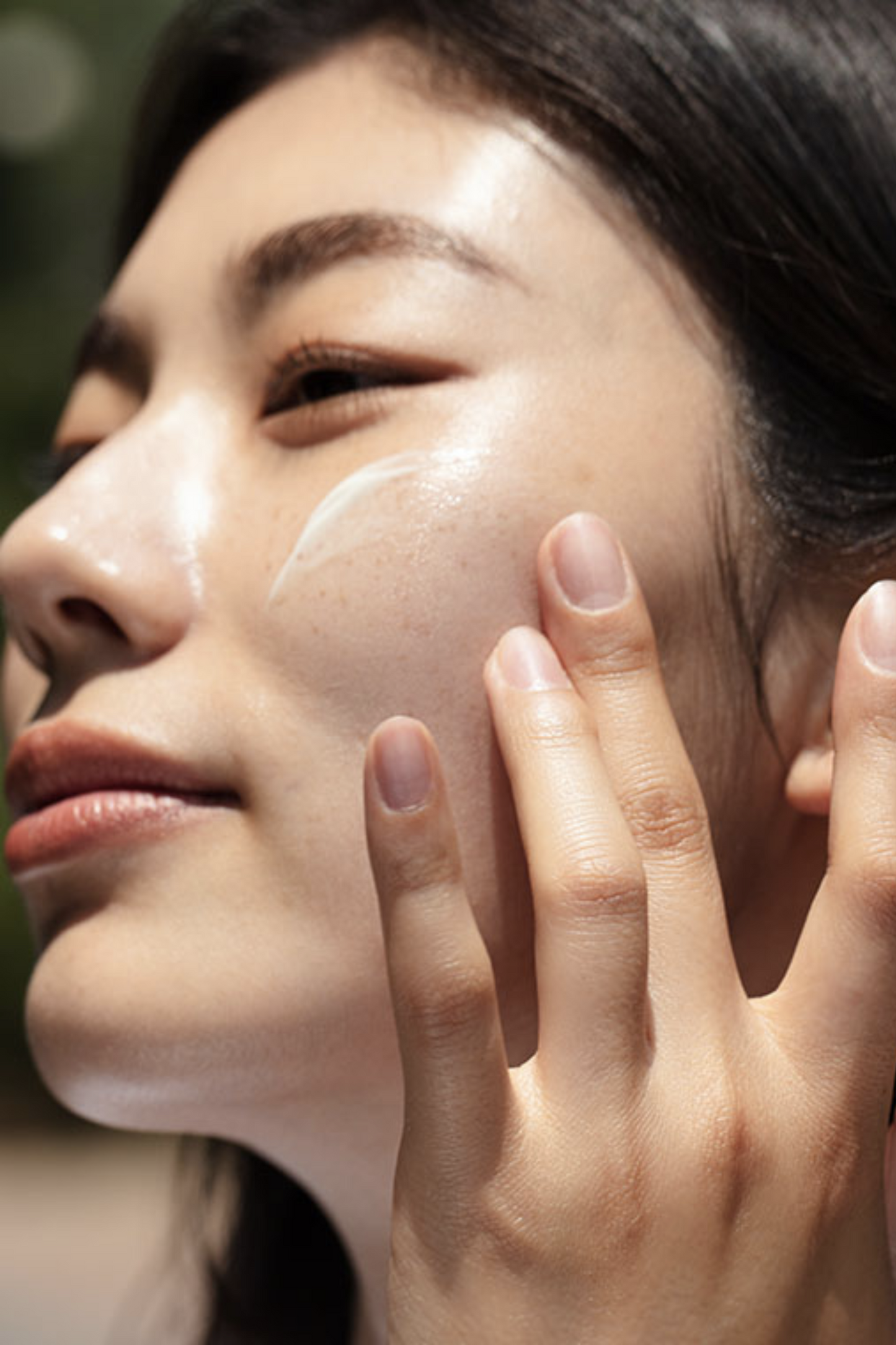 Close up side view of woman's face. Her hand is at her cheek and there is a smear of Klairs All Day Airy Sunscreen visible.