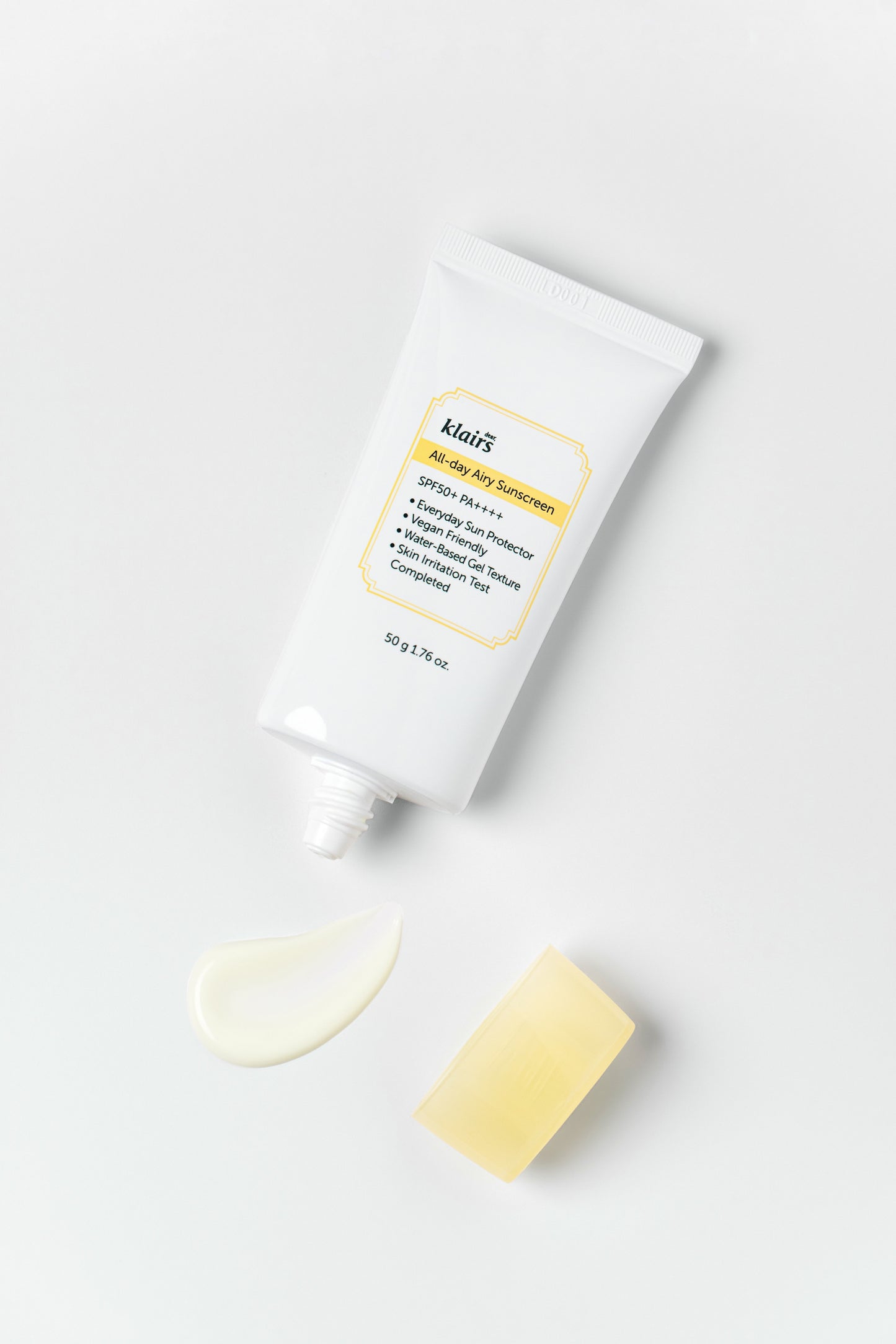 Aerial view of Klairs All Day Airy Sunscreen with its cap off and a smear of sunscreen in front of it, against a white background.