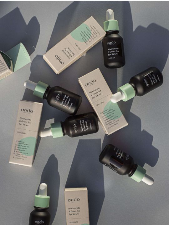 Six bottles of Ondo Beauty Niacinamide & Green Tea Eye Serum with their retail boxes on a grey background