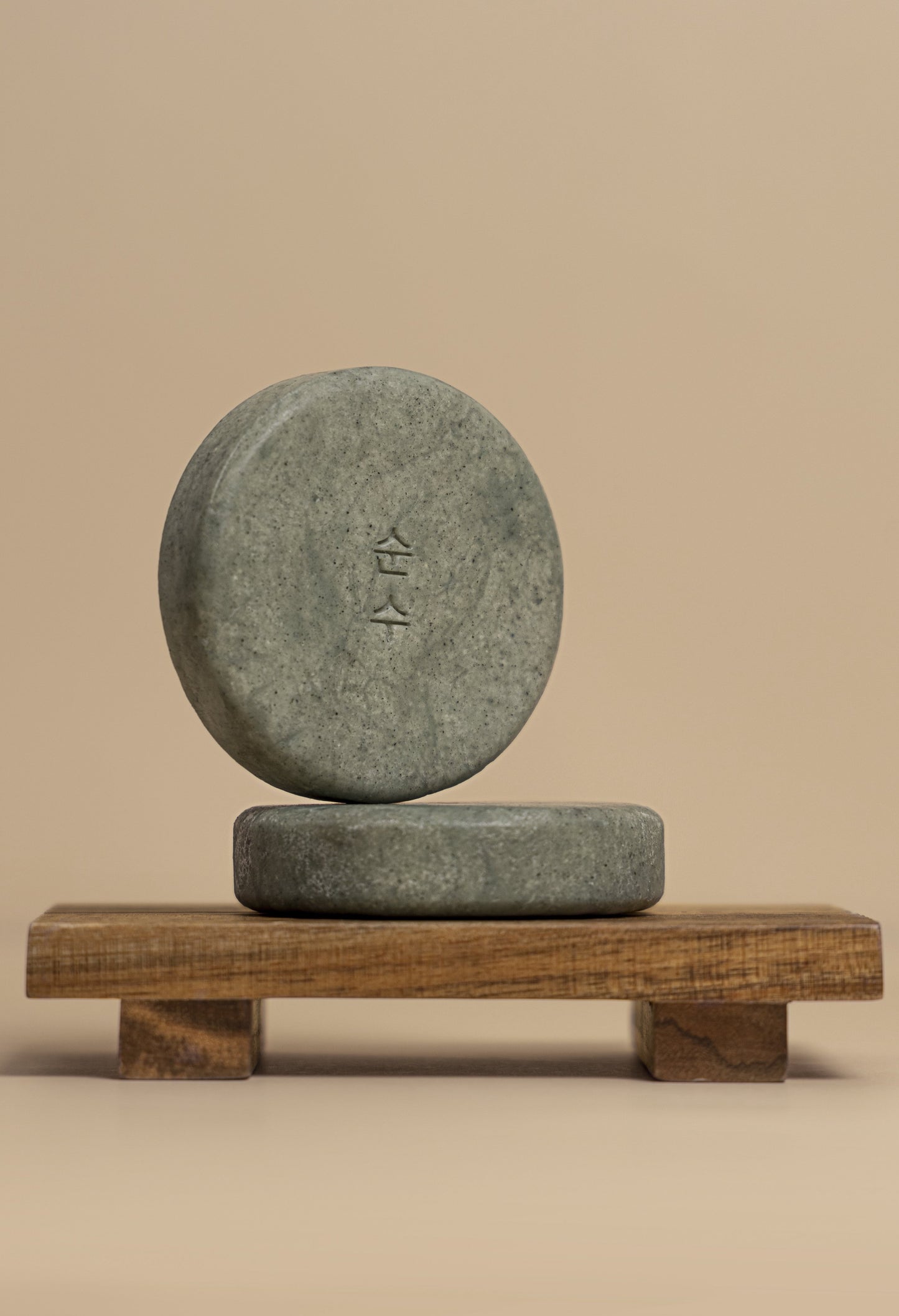 Two of Ondo Beauty 36.5's BHA & Ginger Shampoo Bars on a wooden platform against a beige background. One bar is on its side lying flat, with the other bar standing on top of it.