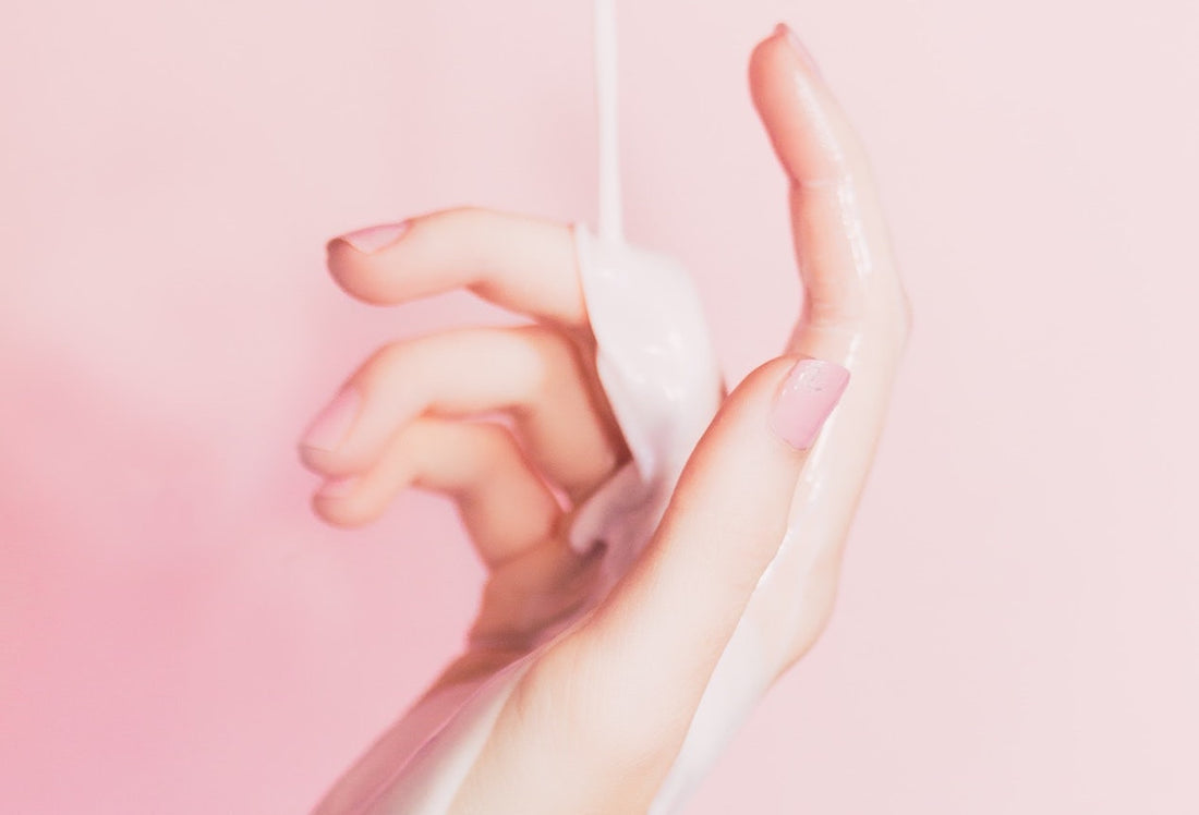 Moisturizing lotion being poured onto hand against pink background