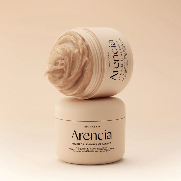 One open jar of Arencia Calendula Rice Mochi Cleanser tipped on its side on top of a closed jar - on a beige background