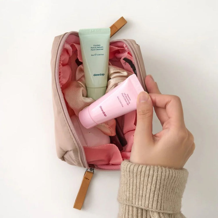 Woman reaching into pouch to pick up mini tubes of Dewdap's Cicatea cleanser and Dewtox cleanser