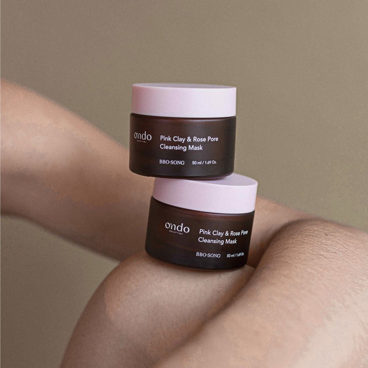 Two jars of Ondo Beauty Pink Clay Rose Pore Clarifying Mask against bare skin and neutral background