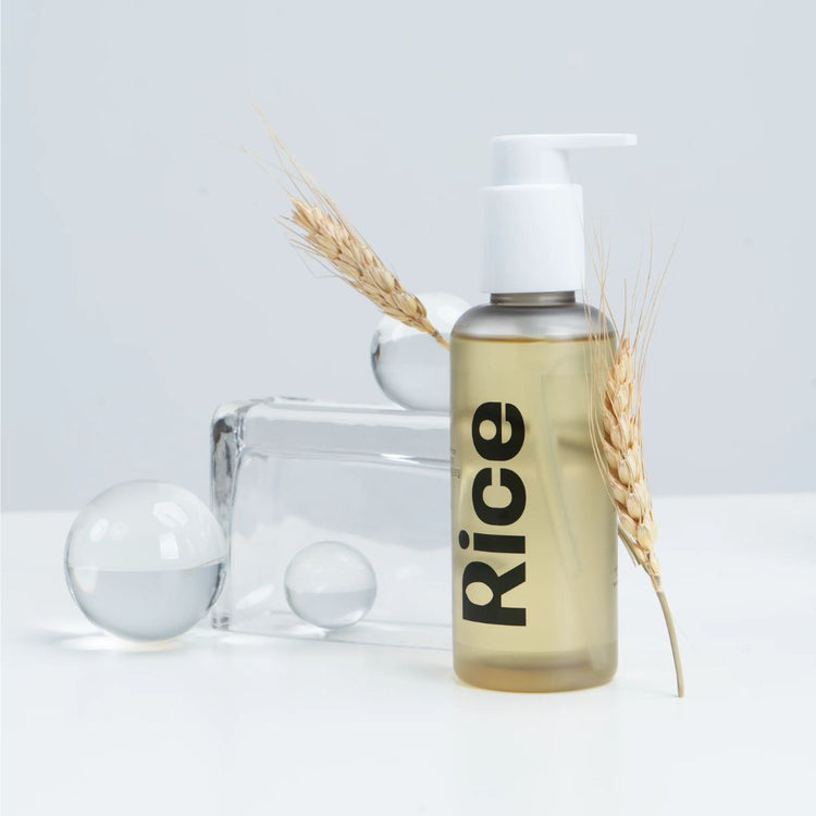 Bottle of Vegreen Rice Cleansing Oil with grain and transparent spheres - on a light grey background