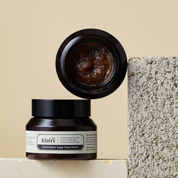 Two jars of Klairs Gentle Black Sugar Facial Polish on a beige background with grey stone