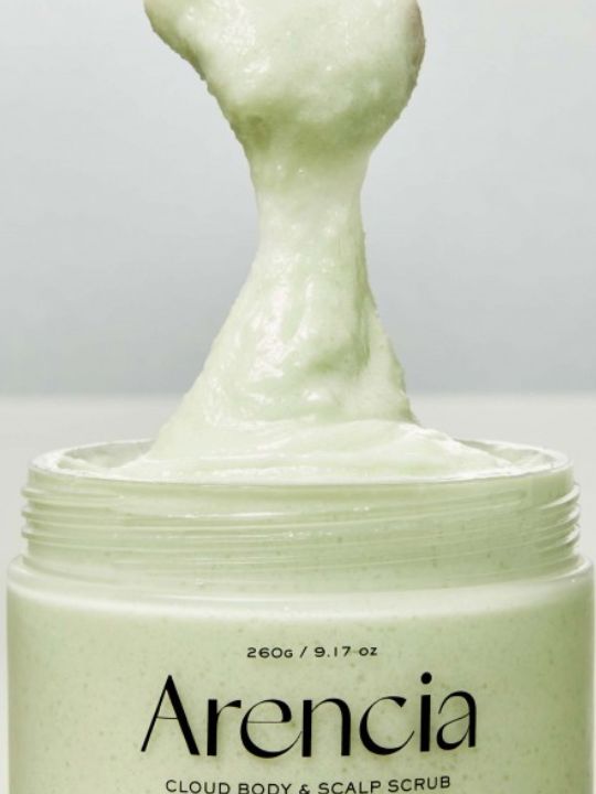 A close-up of a jar of Arencia Cloud Body & Scalp Scrub Geranium & Primrose, showing a thick, pale green scrub being lifted from the open container against a light gray background.