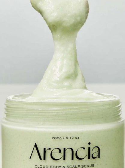 A close-up of a jar of Arencia Cloud Body & Scalp Scrub Geranium & Primrose, showing a thick, pale green scrub being lifted from the open container against a light gray background.