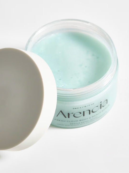 An open jar of Arencia Cloud Body & Scalp Scrub French Mint & Lily with a white lid leaning against it, showing a pale mint green balm inside on a clean white background.