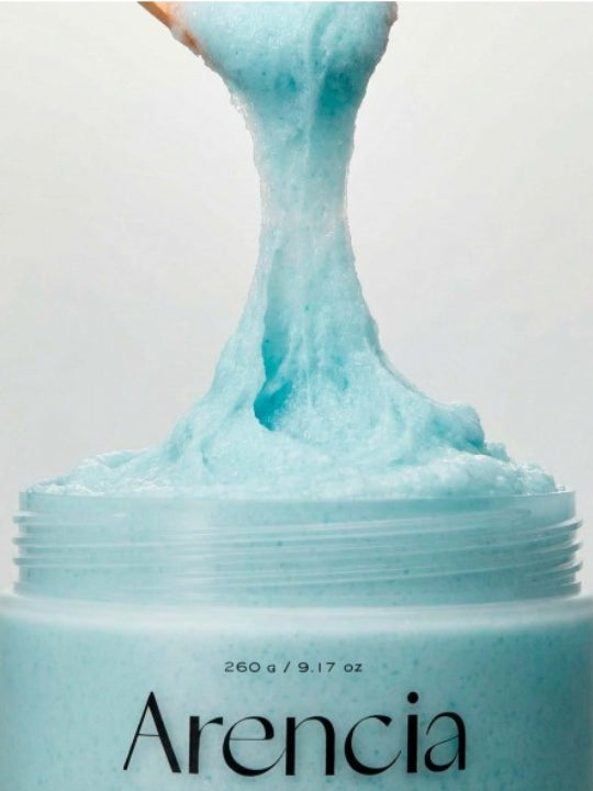 A close-up of a textured Arencia Cloud Body & Scalp Scrub French Mint & Lily  being lifted from a jar against a plain light background.