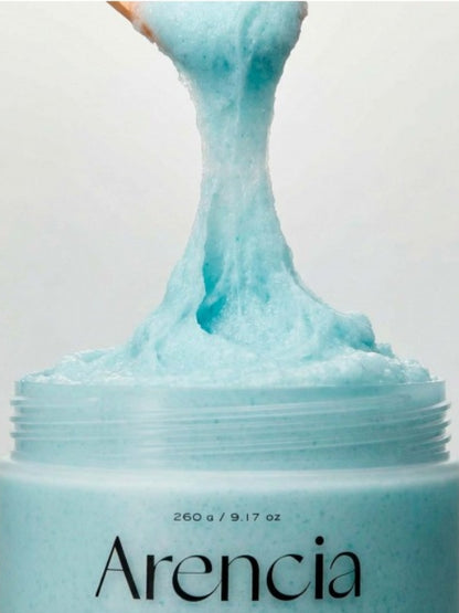 A close-up of a textured Arencia Cloud Body & Scalp Scrub French Mint & Lily  being lifted from a jar against a plain light background.