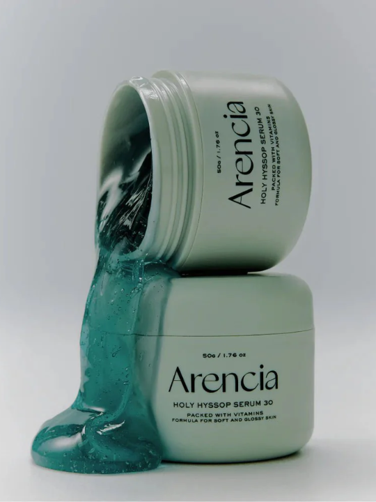 Two jars of Arencia Holy Hyssop Serum 30 with green serum spilling out on a light gray background