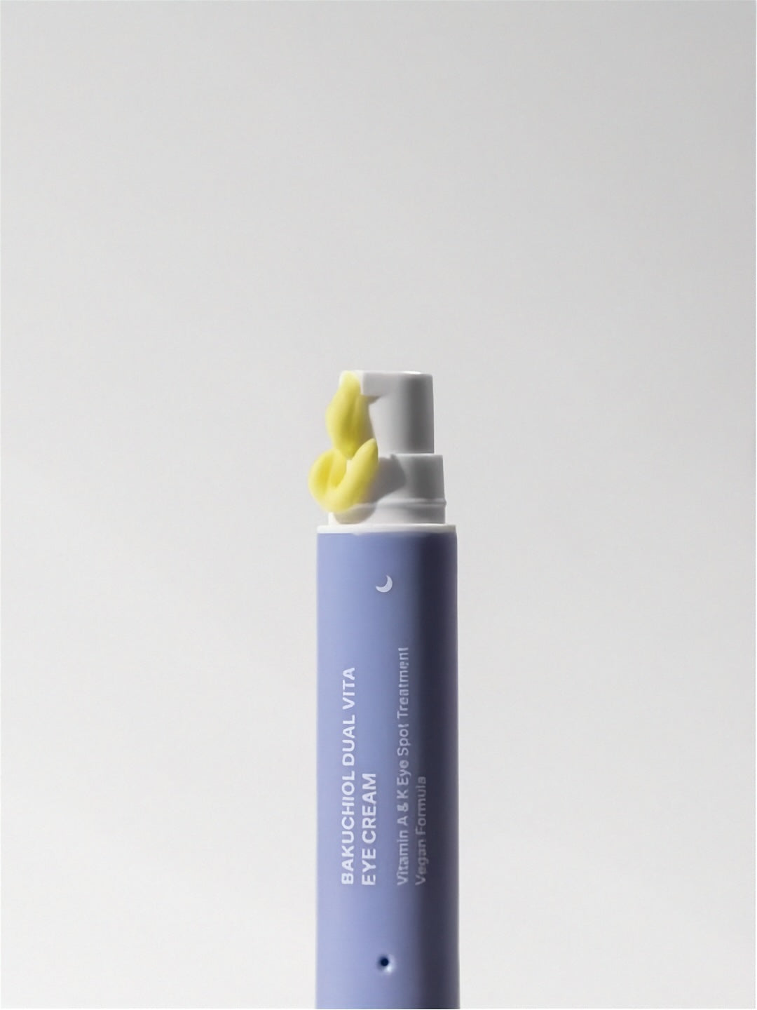 Tube of Herbloom Bakuchiol Dual Vita Eye Cream with yellow cream being pumped out on a white background.