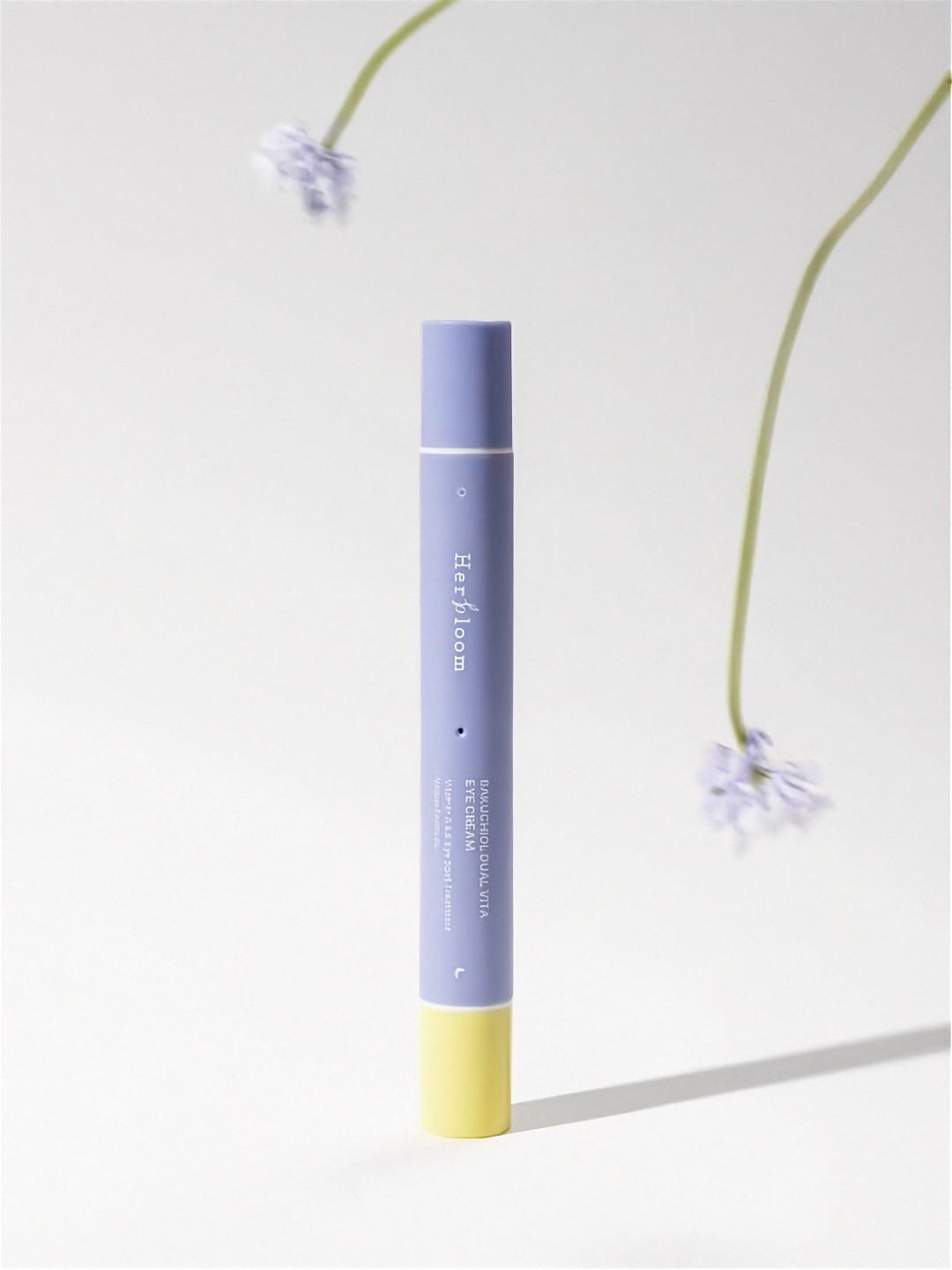 Purple and yellow tube of tube of Herbloom Bakuchiol Dual Vita Eye Cream on a light gray background with floral elements.