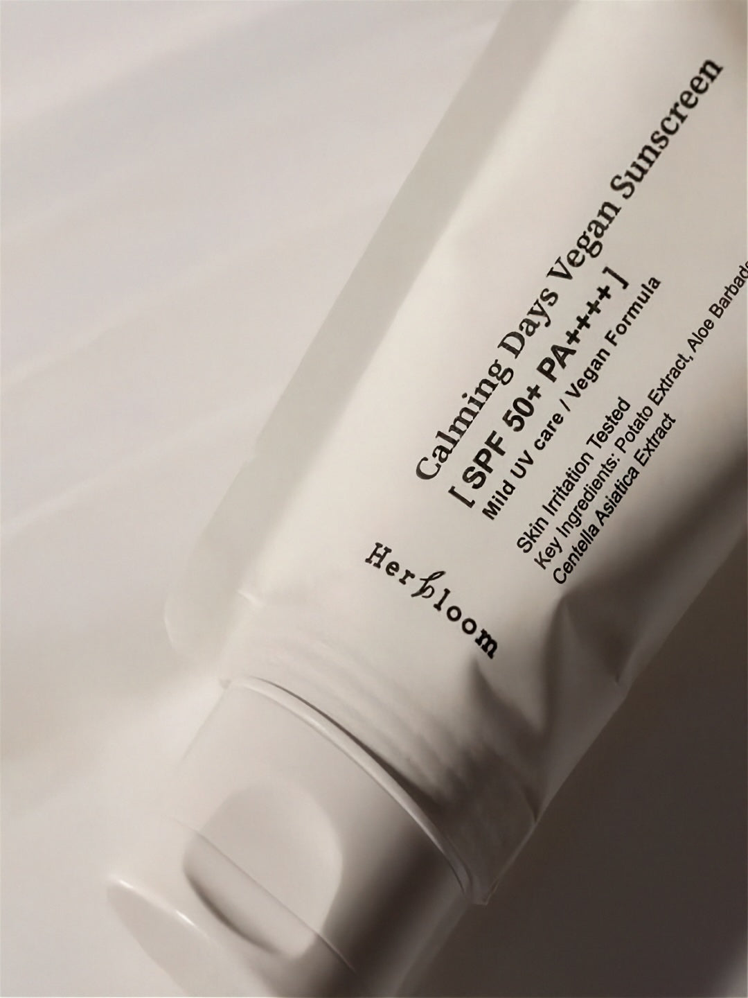 Close up of Herbloom Calming Days Vegan Sunscreen SPF 50+ tube in low light on a white background