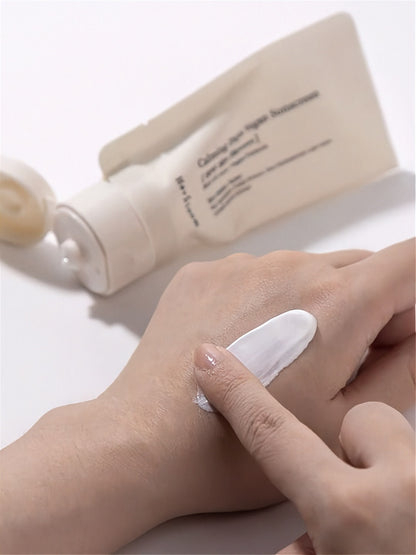 Finger applying white cream to a hand with tube of Herbloom Calming Days Vegan Sunscreen in the background.
