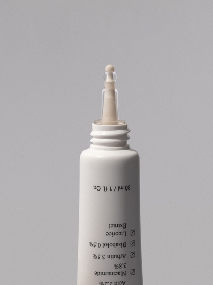Ondo Beauty's Tranexamic Acid & Licorice Dark Spot Treatment uncapped with a drop squeezed out, against a grey background.