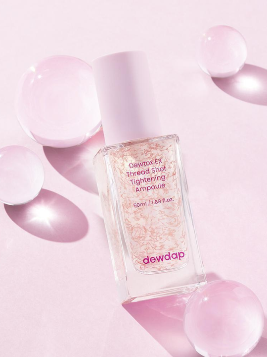 Bottle of Dewdap Detox Ex Thread Shot Tightening Ampoule on a light pink background with four clear spheres.