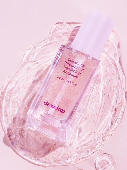 Bottle of Dewdap Detox Ex Thread Shot Tightening Ampoule laying face up on a swatch of serum on a pink background. Available at Sinless Skincare.