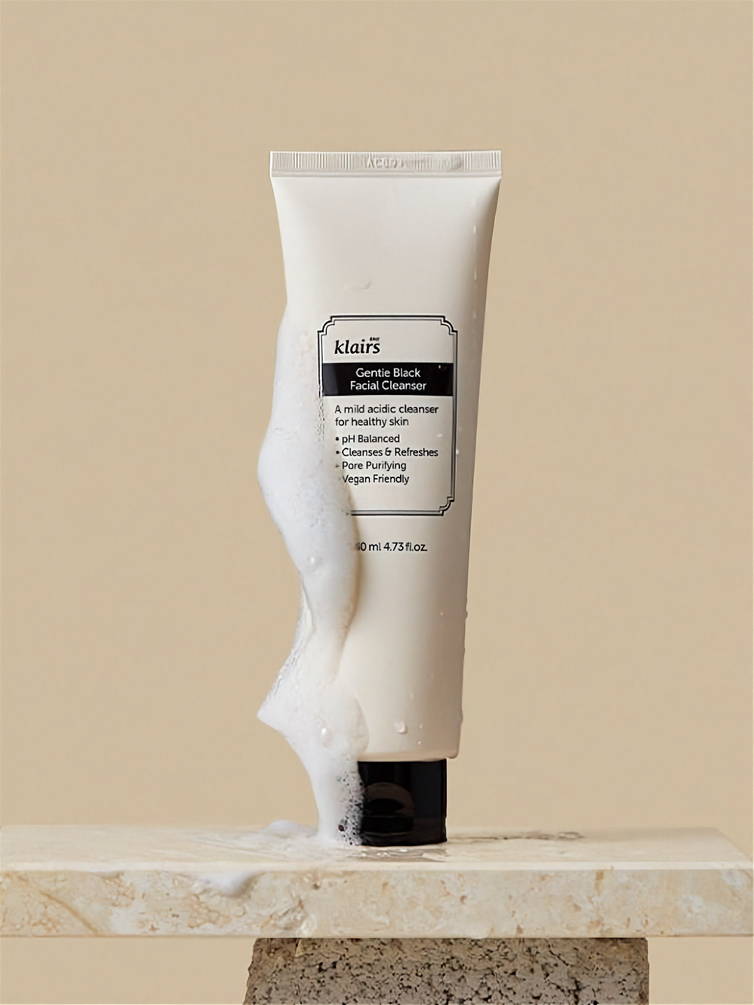 Klairs Gentle Black Facial Cleanser with foam running down one side of the tube, on a stone surface, against a beige background.