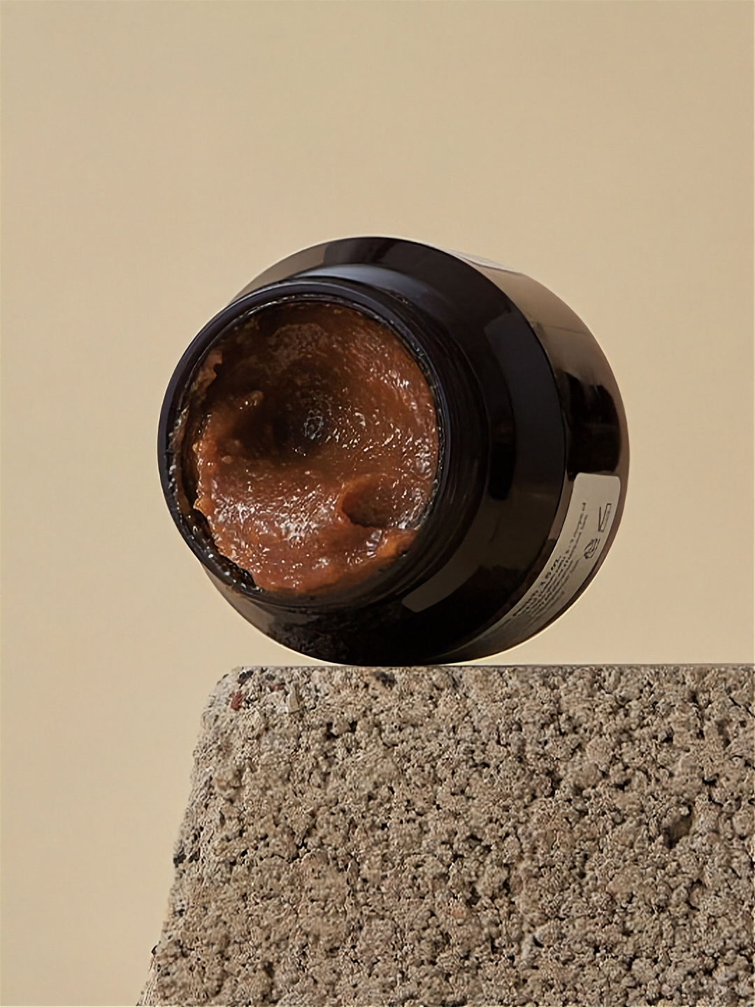Open jar of Klairs Gentle Black Facial Polish on a textured stone surface against a beige background