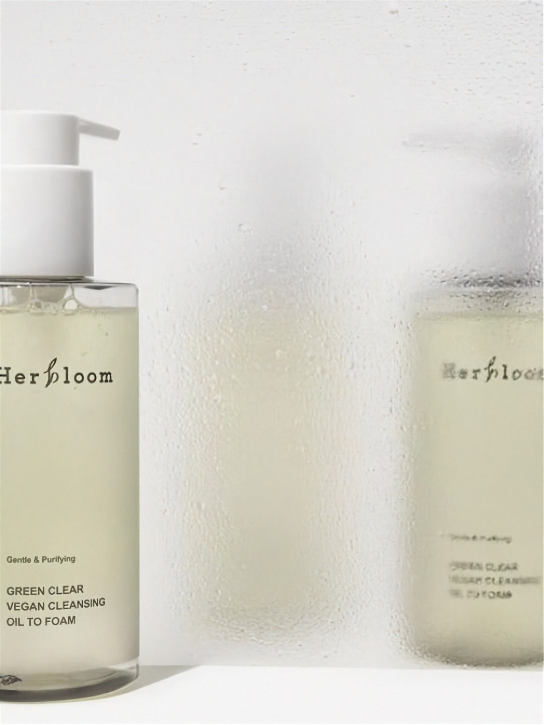 Two bottles of Herbloom Green Clear Vegan Cleansing Oil to Foam on a white background with condensation and water droplets