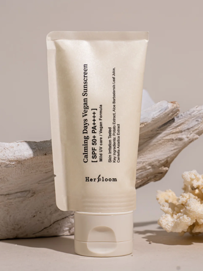 Tube of Herbloom Calming Days Vegan Sunscreen in front of a piece of driftwood, against a beige background. Available at Sinless Skincare Switzerland.