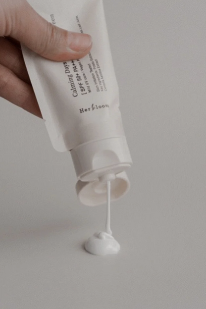 An open bottle of Herbloom's Calming Days Vegan Sunscreen is being squeezed upside down onto a light grey surface.