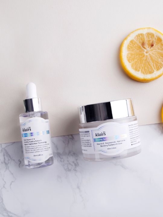 Klairs Freshly Juiced Vitamin Drop and Vitamin E Mask lying on a marble surface with an orange slice