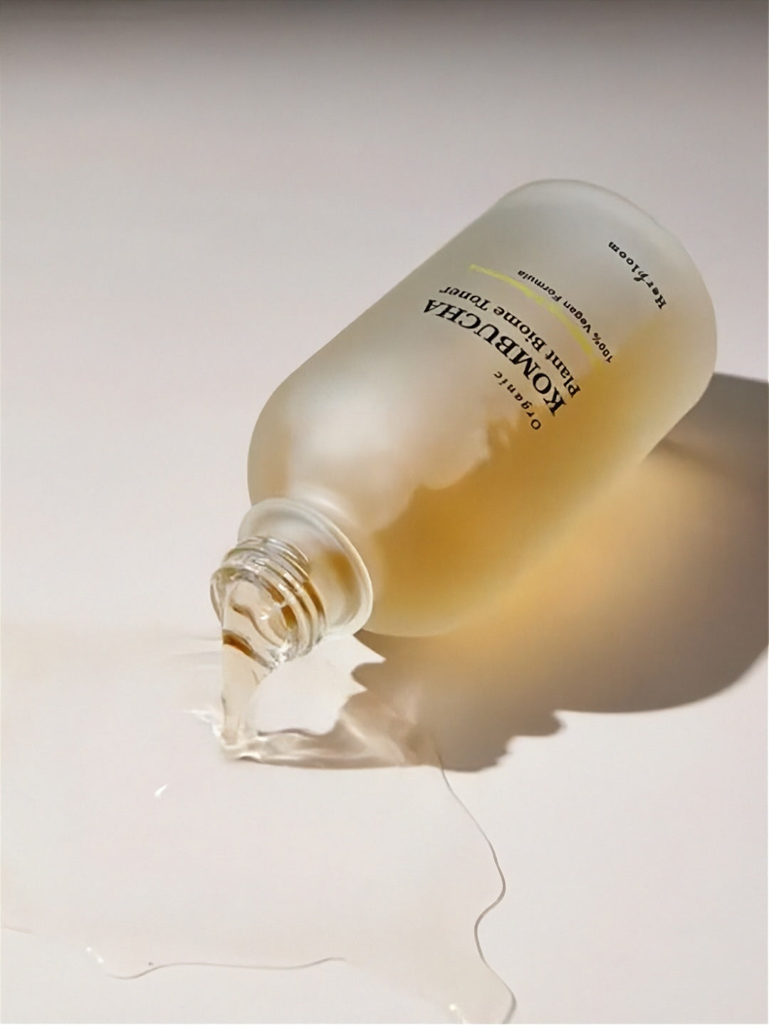 Herbloom Kombucha Plant Biome Toner bottle tipped over with liquid pouring out on a neutral grey surface