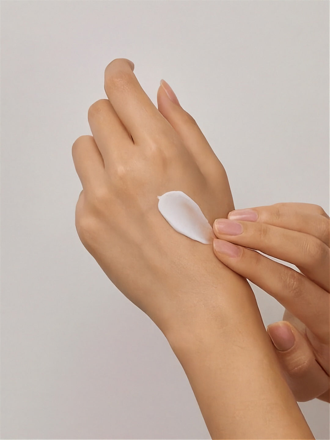 Hand applying a small amount of Herbloom's Kombucha Vegan Collagen Cream to another hand against a light grey background