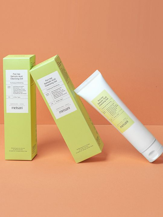 Tube of Meisani Puri-Tea Salicylic Acid Cleansing Gel leaning on its packaging - on an orange background