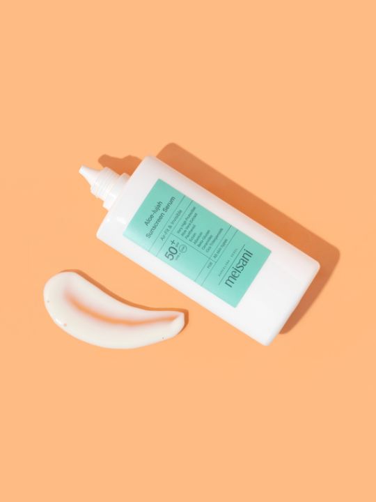 Open tube of Meisani Aloe-lujah Sunscreen Serum laying on an orange surface with a smear of product 