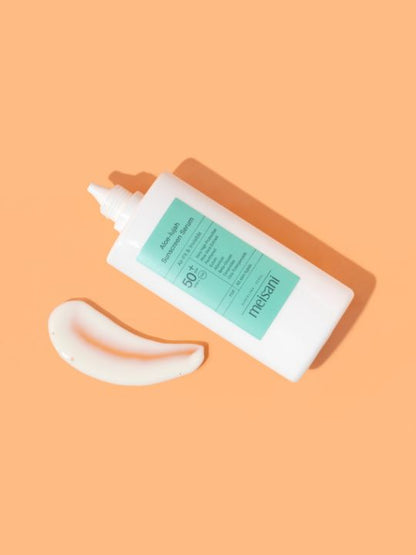 Open tube of Meisani Aloe-lujah Sunscreen Serum laying on an orange surface with a smear of product 