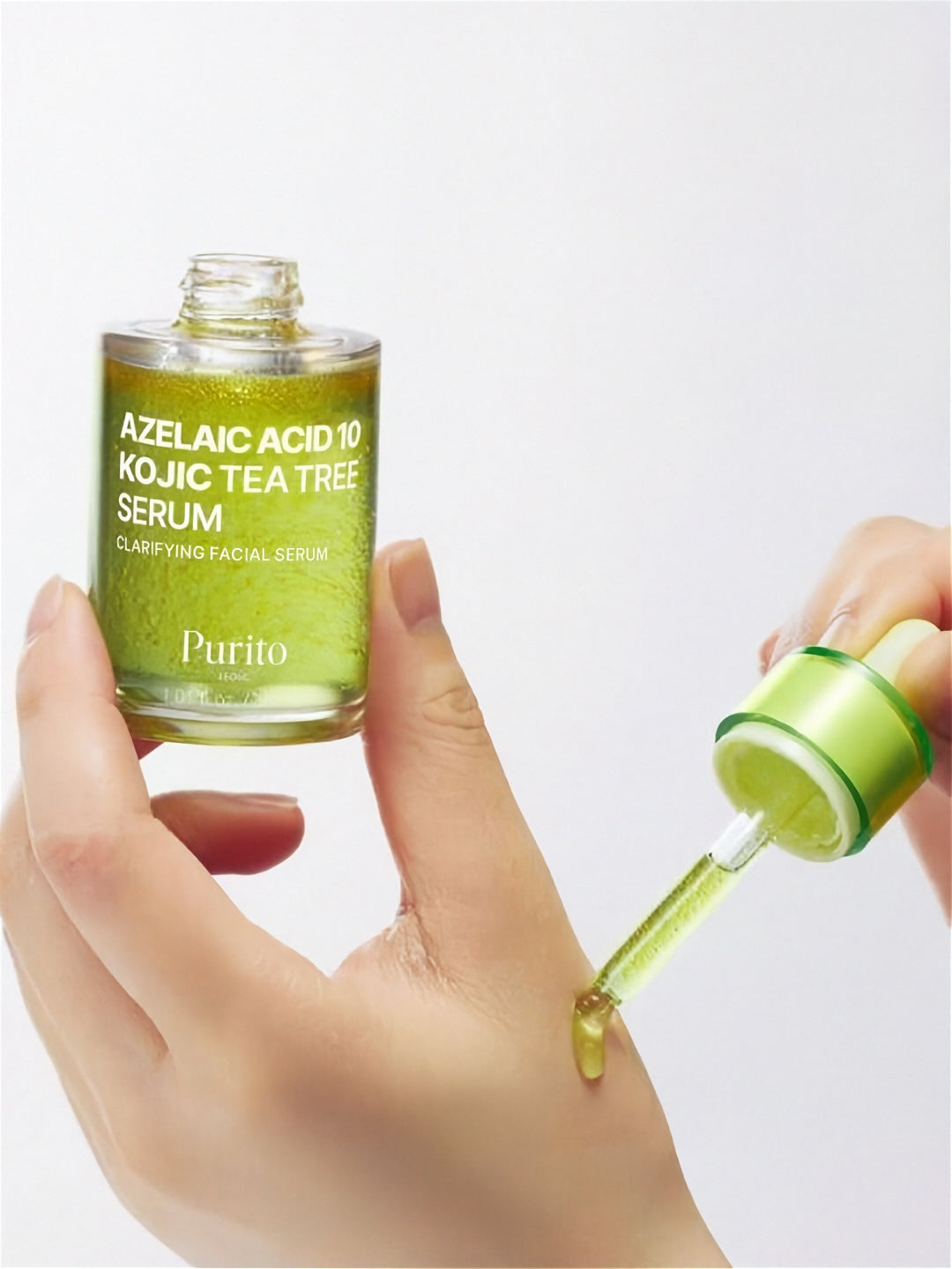 Hand applying Purito Seoul Azelaic Acid 10 Kojic Tea Tree Serum with a dropper to the other hand, on a light grey background