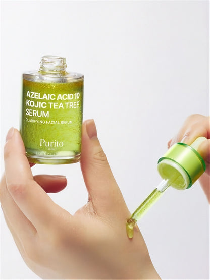 Hand applying Purito Seoul Azelaic Acid 10 Kojic Tea Tree Serum with a dropper to the other hand, on a light grey background