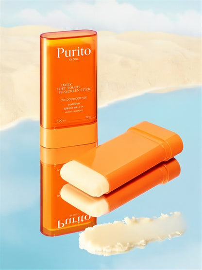 Two tubes of Purito Seoul Daily Soft Touch Sunscreen Stick with on one its side without its cap, and a swatch of white cream on a reflective blue surface