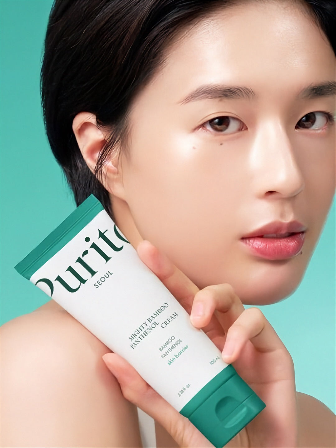 Woman holding a tube of Purito Mighty Bamboo Panthenol Cream against a teal background