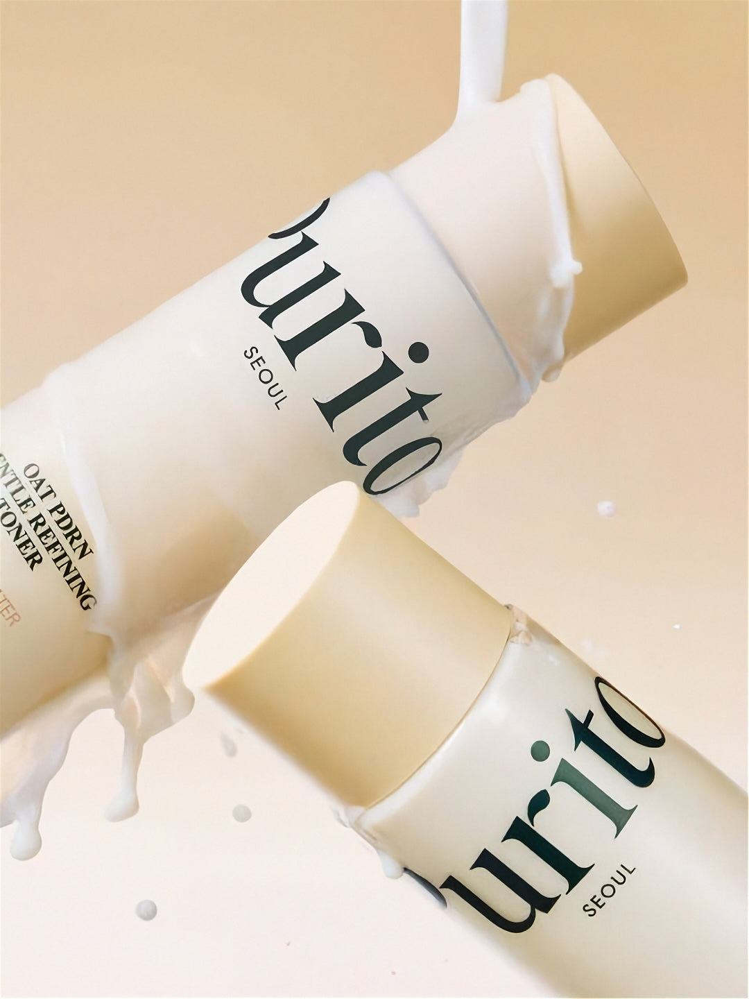 Two bottles of Purito Oat PDRN Gentle Refining Toner with white liquid running down, on a beige background
