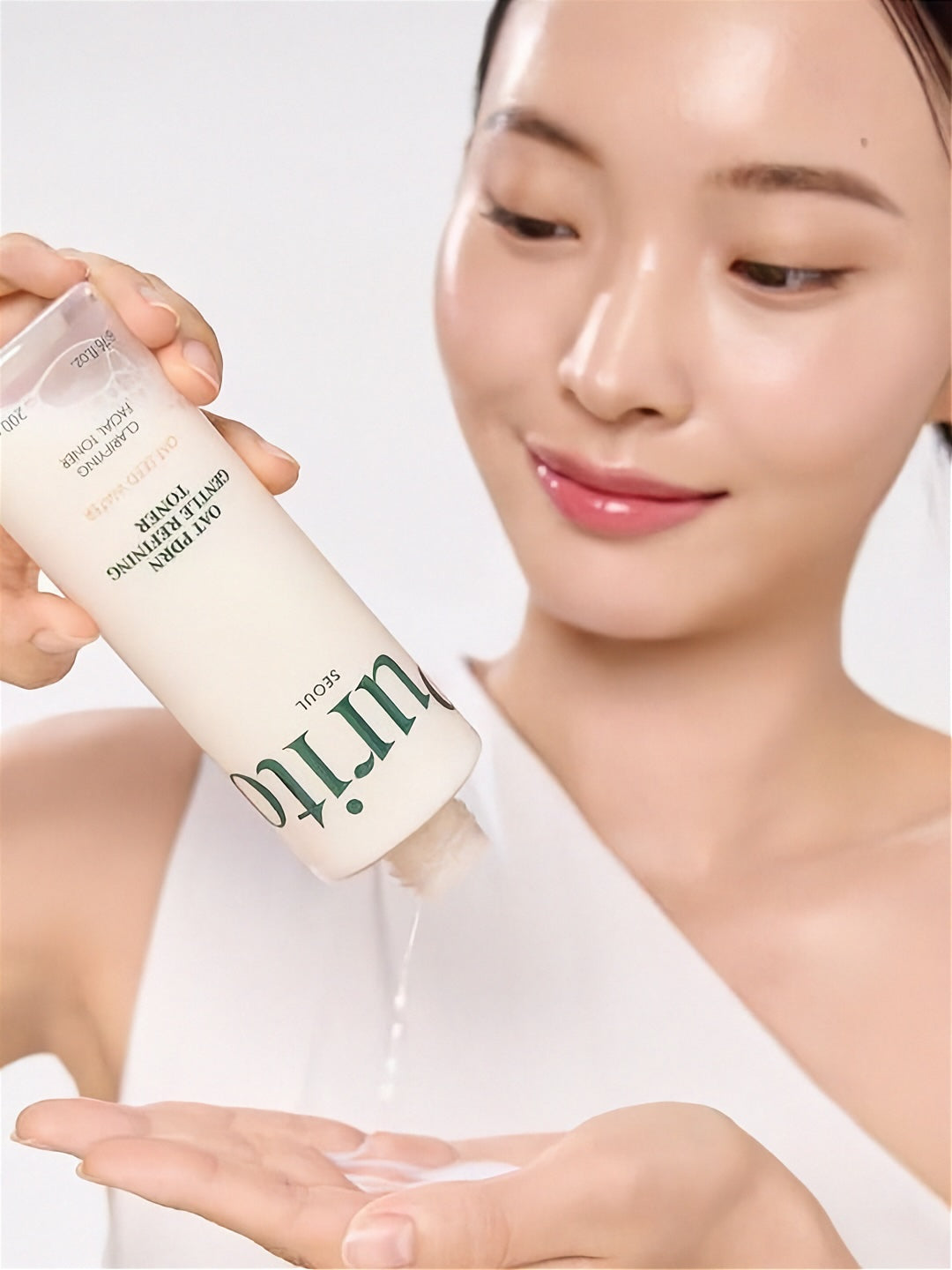 Woman pouring liquid from a bottle of Purito Oat PDRN Gentle Refining Toner onto her hand against a white background