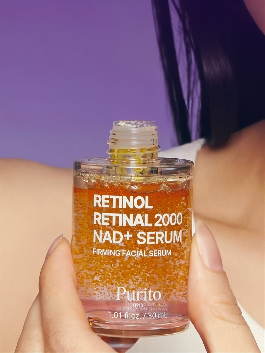 Open bottle of Purito Retinol Retinal 2000 NAD+ Serum held by a person against a purple background