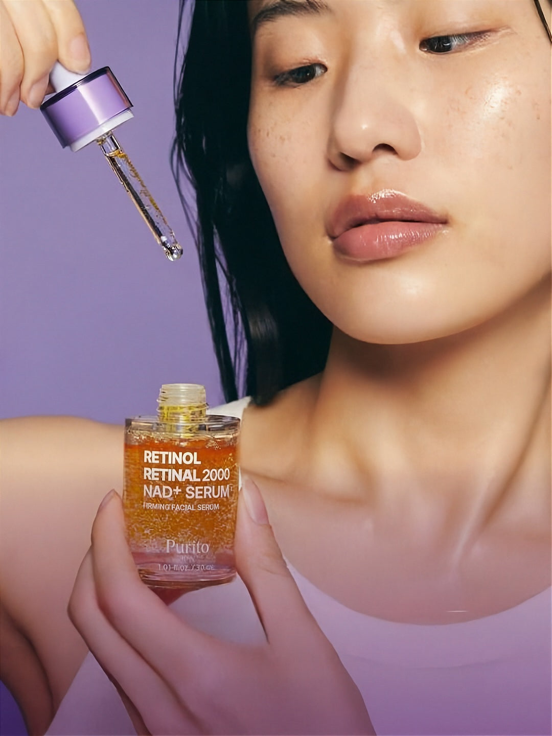 Woman holding a bottle of Purito Retinol Retinal 2000 NAD+ Serum with dropper out against a purple background