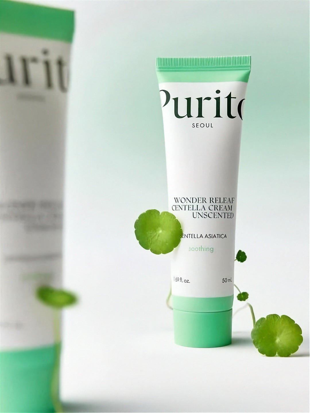Two tubes of Purito Wonder Releaf Centella Unscented Cream, one tube is blurred, with cica plants, on a light gradient green background